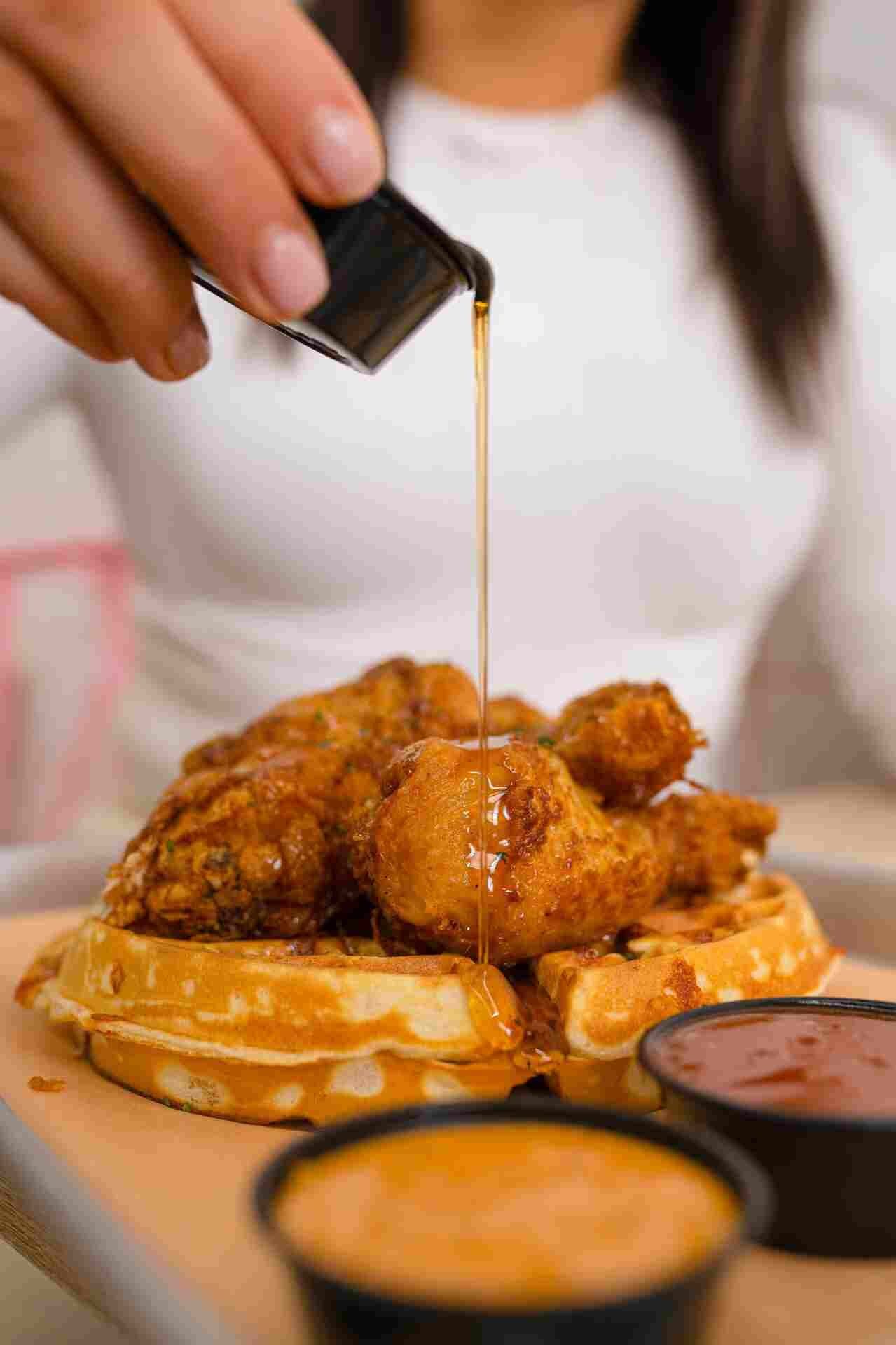 68c84ebd2bb46_Hand pouring syrup on chicken and waffles